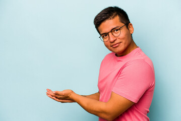 Young hispanic man isolated on blue background holding a copy space on a palm.
