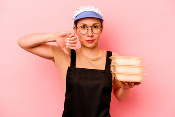 Young cook volunteer woman isolated on pink background showing a dislike gesture, thumbs down....