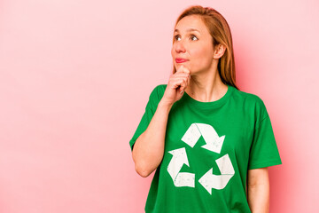 Young volunteer woman isolated on pink background looking sideways with doubtful and skeptical...