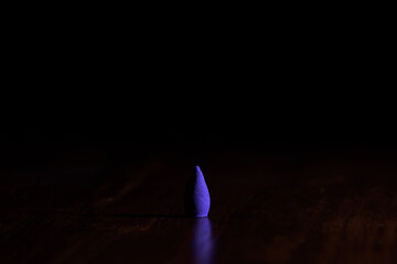 Violet incense cone on a wooden surface with a dark background.