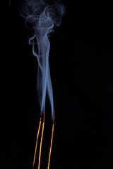 Close-up image of three golden-colored incense sticks burning and blue smoke rising to the top. Copy Space.