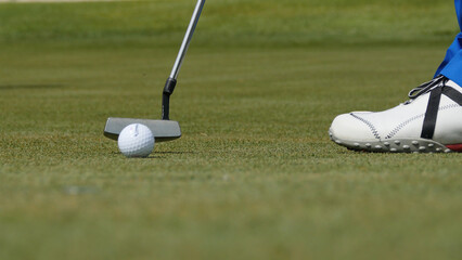 Professional golfer putting ball into the hole. Golf ball by the edge of hole with player in background on a sunny day