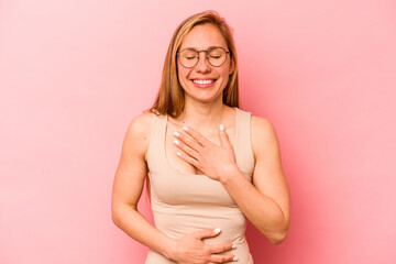 Young caucasian woman isolated on pink background laughs happily and has fun keeping hands on...