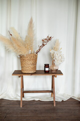 Scandinavian style living room interior with furniture. Cozy design room home: on wooden table wicker basket with dried flowers, candle and vase with pampas grass, spikelets. Interior workspace home. 
