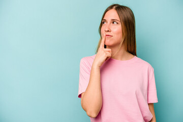 Young caucasian woman isolated on blue background looking sideways with doubtful and skeptical expression.