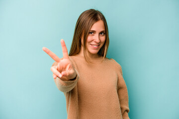 Young caucasian woman isolated on blue background joyful and carefree showing a peace symbol with...