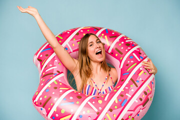 Young caucasian woman holding air mattress isolated on blue background