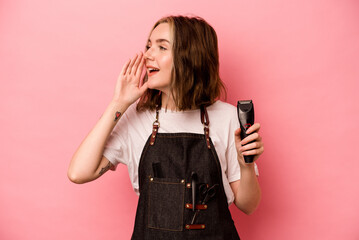 Young hairdresser woman holding scissors isolated on pink background shouting and holding palm near opened mouth.