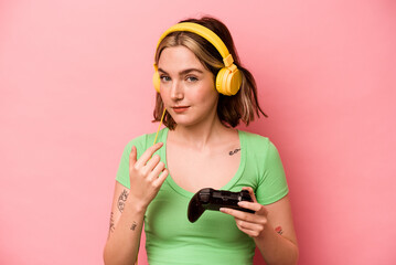 Young caucasian woman playing with a video game controller isolated on pink background pointing with finger at you as if inviting come closer. © Asier