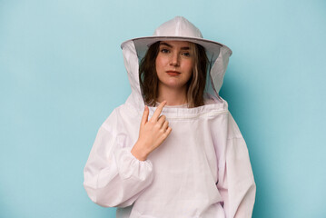 Young caucasian beekeeper woman isolated on blue background pointing with finger at you as if inviting come closer.