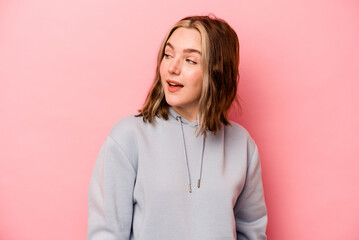 Young caucasian woman isolated on pink background looks aside smiling, cheerful and pleasant.