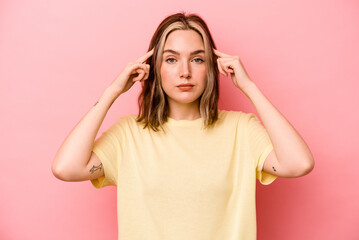 Young caucasian woman isolated on pink background focused on a task, keeping forefingers pointing head.