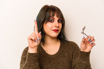 Obraz premium Young caucasian makeup artist woman holding a eyelash curler isolated on white background showing number one with finger.