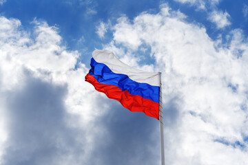 Russian white-blue-red flag is waving in front of blue sky and clouds