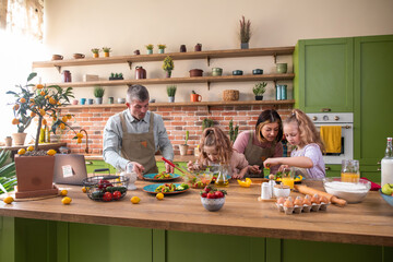 Happy two kids girls have a fun time with their parents at the kitchen island they prepare together the dinner the little girl helping her mom to cook some delicious food