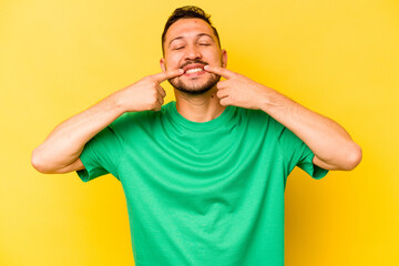Fototapeta na wymiar Young hispanic man isolated on yellow background smiles, pointing fingers at mouth.