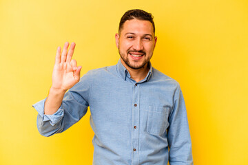 Young hispanic man isolated on yellow background cheerful and confident showing ok gesture.