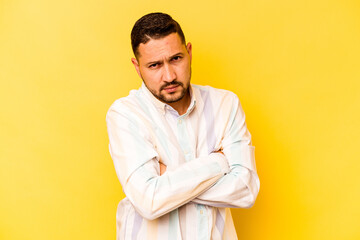 Young hispanic man isolated on yellow background frowning face in displeasure, keeps arms folded.