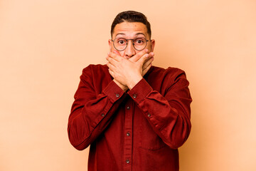 Young hispanic man isolated on beige background shocked covering mouth with hands.