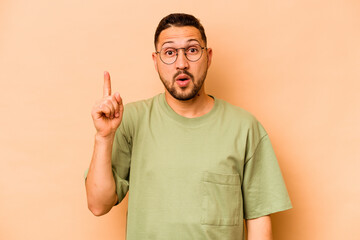 Young hispanic man isolated on beige background pointing upside with opened mouth.