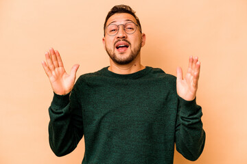Young hispanic man isolated on beige background laughs out loudly keeping hand on chest.