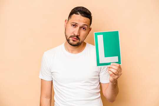 Hispanic man holding a beginner driver sign isolated on beige background