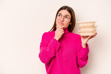 Young caucasian woman holding tupperware isolated on white background looking sideways with...