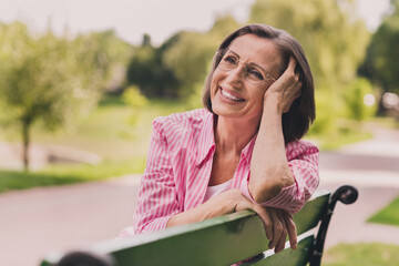 Photo of adorable dreamy lady pensioner wear pink shirt sitting park bench smiling outdoors...