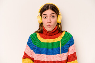 Young caucasian woman listening to music isolated on white background shrugs shoulders and open eyes confused.