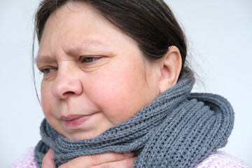 close-up of mature woman 55 years face, sick person with inflamed eyes holding on to sore throat,...