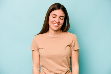 Young caucasian woman isolated on blue background laughs and closes eyes, feels relaxed and happy.