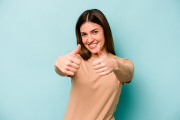 Young caucasian woman isolated on blue background raising both thumbs up, smiling and confident.