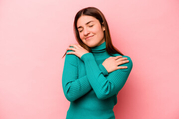 Obraz premium Young caucasian woman isolated on pink background hugs, smiling carefree and happy.