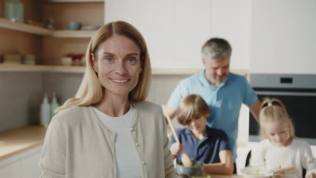 Beautiful caucasian woman standing in the kitchen and smiling to the camera. Beautiful family with little kids prepare breakfast together at home.