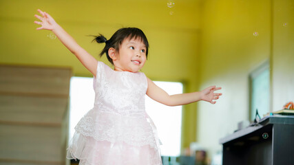 Happy Little girl playing soap bubbles in living room.