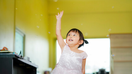 Fototapeta na wymiar Happy Little girl playing soap bubbles in living room.