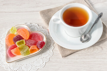 A cup of tea with delicious jelly multi-colored marmalade on a white plate.