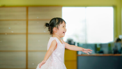 Happy Little girl playing soap bubbles in living room.