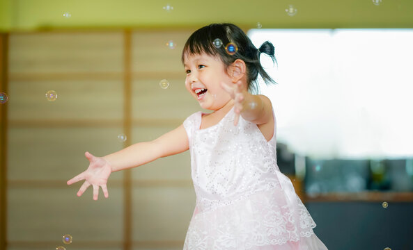 Happy Little girl playing soap bubbles in living room.