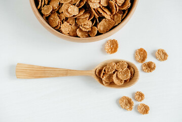 Crispy healthy dry cereal flakes in a wooden bowl with wooden spoon on white background