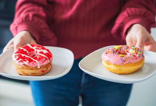A woman holding and serving two tasty pink donuts on a plate