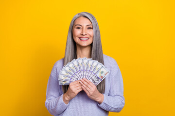 Photo of cheerful good mood lovely grandma lottery winner hold many dollars isolated on yellow color background