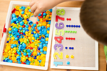 By provided numbers boy inserting pins. counting game. mathematical task. play at home. way of learning.