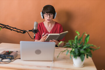 Portrait of mature woman wearing headphones and talking at online radio station - podcast and...