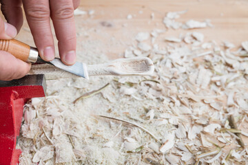 Selbst geschnitzter Holzlöffel eingespannt im Schraubstock bearbeitet mit Messer Werkzeug auf einer Werkbank mit Holzspäne, Deutschland - obrazy, fototapety, plakaty