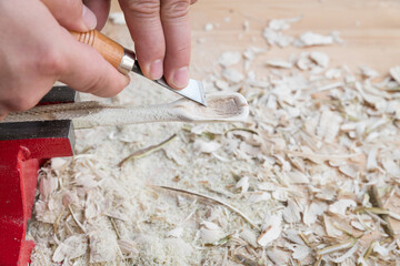Selbst geschnitzter Holzlöffel eingespannt im Schraubstock bearbeitet mit Messer Werkzeug auf einer Werkbank mit Holzspäne, Deutschland