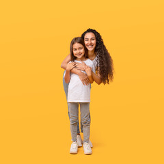 Happy Arabic Mother Hugging Little Daughter Standing Over Yellow Background