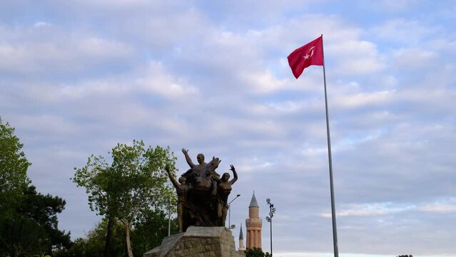 Anatalya, Turkey. 19 December 2021: Turkish flag waving in blue sky , Republic Square in Antalya. A lively town square with equestrian statue of former President Ataturk surrounded by numerous cafes.