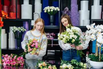 Fototapeta premium Two young women take orders by phone and make beautiful festive bouquets in a cozy flower shop. Floristry and bouquet making in a flower shop. Small business.