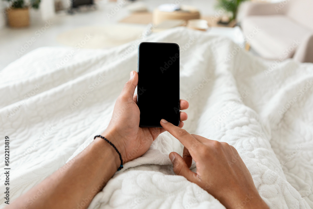 Poster man texting on smartphone with blank screen in bedroom, pov